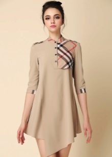 Ang murang beige na damit na may isang asymmetrical ilalim na may isang checkered insert sa dibdib